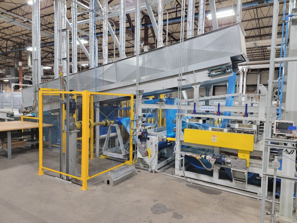 Yellow safety cage surrounds a blue and gray coating line with layered conveyor systems, set within a spacious industrial environment.