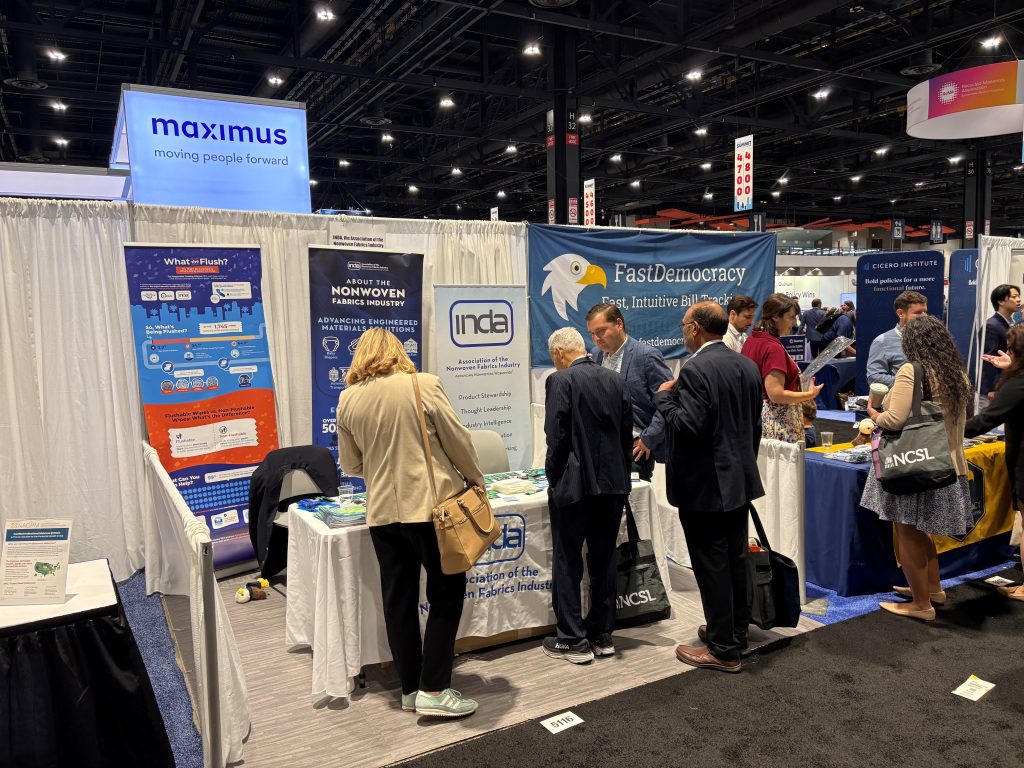 A trade show booth featuring INDA and FastDemocracy, with attendees engaged in discussion among banners and informational displays.